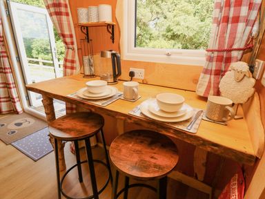 A wooden breakfast bar with two stools set with plates bowls and mugs next to a window at Shepherd's Cwtch in Cilycwm near Llandovery