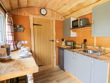 A kitchen with wooden ceiling and door a countertop with a stainless steel sink grey cabinets microwave and toaster at Shepherd's Cwtch in Cilycwm near Llandovery