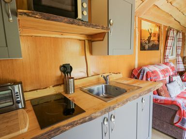 A kitchen area with a sink stovetop utensils and toaster next to a sofa with red plaid covers at Shepherd's Cwtch in Cilycwm near Llandovery