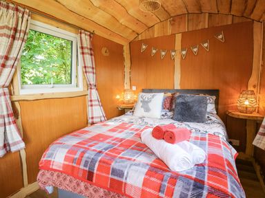 A bedroom with a bed covered with pillows and folded towels next to a window with curtains at Shepherd's Cwtch in Cilycwm near Llandovery