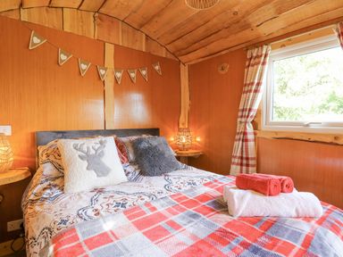 A bedroom with a bed leggings patterned bedding and pillows beside a window at Shepherd's Cwtch in Cilycwm near Llandovery