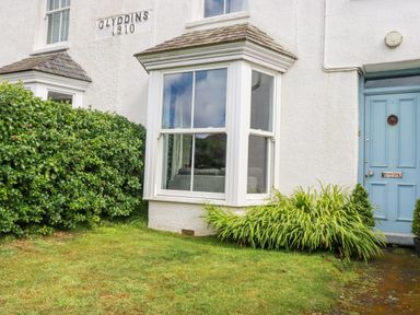 Exterior of a white house with a bay window blue door and plants in the garden at 2 Glyddins 1910 in Rock