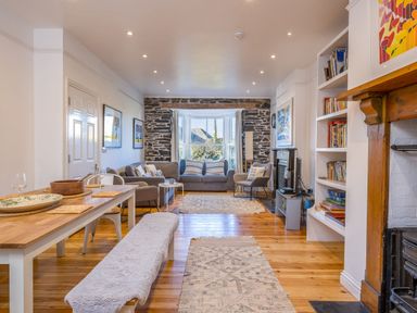 A living room with wooden floor a dining table with a bench and chairs sofas and a stone wall with windows at 2 Glyddins 1910 Rock