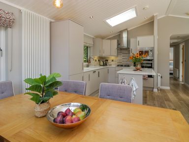 A kitchen and dining area with a wooden table and fruit bowl at Waterside Lodge 55A Bowness White Cross Bay near Windermere