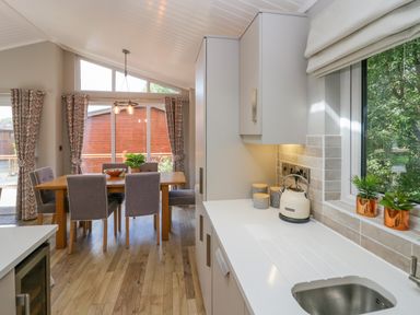 A kitchen with a white countertop and sink next to a dining table with six chairs at Waterside Lodge 55A Bowness White Cross Bay near Windermere