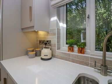 A kitchen countertop with a white kettle three canisters two small plants on the windowsill and a faucet at Waterside Lodge 55A Bowness White Cross Bay near Windermere