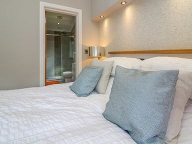 A bedroom with a bed and cushions and a view of an en suite bathroom at Waterside Lodge 55A Bowness White Cross Bay near Windermere