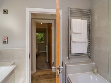 A bathroom with a towel rack holding white towels and a bathtub next to a doorway showing a hallway at Waterside Lodge 55A Bowness White Cross Bay near Windermere