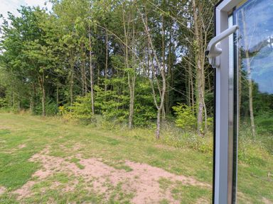 A view of trees and grassland seen through an open glass door at Peacock Lodge in Swannington near Coalville