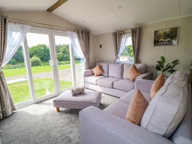 A living room with two sofas an ottoman and large sliding glass doors at Peacock Lodge in Swannington near Coalville