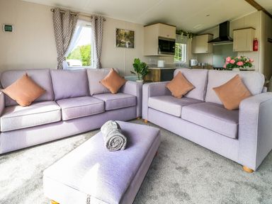 A living room with two sofas and an ottoman with rolled blanket and a view into a kitchen at Peacock Lodge in Swannington near Coalville
