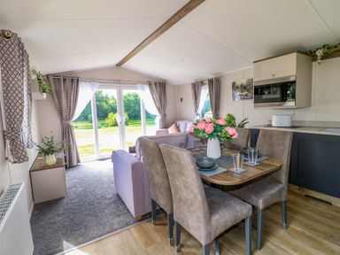 A dining area with table set for four and a living room with sofa and large windows at Peacock Lodge in Swannington near Coalville