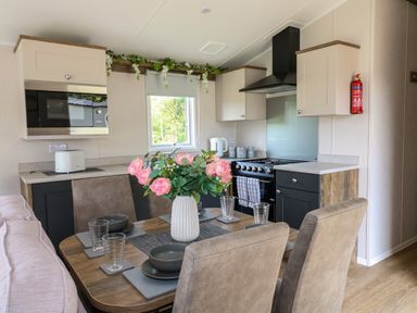 A kitchen and dining area with a table set with plates glasses and a flower vase at Peacock Lodge in Swannington near Coalville
