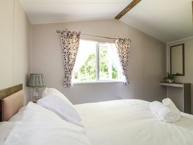 A bedroom with a bed white sheets towels on bed window with patterned curtains lamp on bedside and mirror on wall at Peacock Lodge in Swannington near Coalville