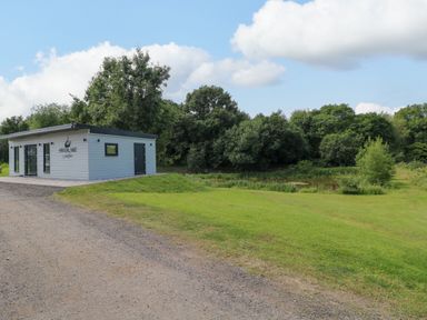 A single story building near a grass field with trees and a pond at Peacock Lodge in Swannington near Coalville