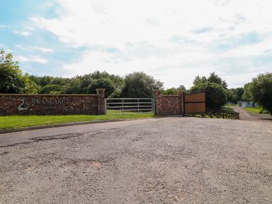 An entrance gate with brick pillars and a metal gate next to a road and greenery at Swanlake Lodges in Swannington near Coalville