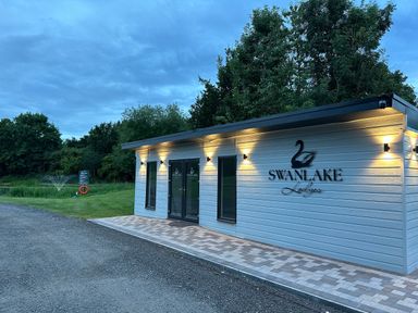A small building with swanlake lodges sign and lights outside near trees and grass at Peacock Lodge Swannington near Coalville