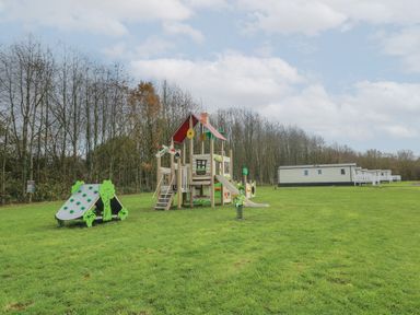 A playground with climbing equipment and a slide on a grassy area near caravans at Peacock Lodge in Swannington near Coalville