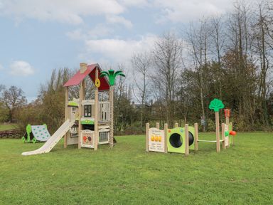 A playground with a slide climbing frame and tunnel on grass near trees at Peacock Lodge in Swannington near Coalville