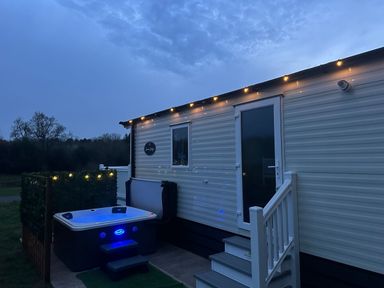 A mobile home with stairs and a hot tub outside at night with string lights at Peacock Lodge in Swannington near Coalville