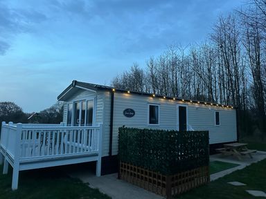 A mobile home with white railings and string lights next to bare trees at Peacock Lodge in Swannington near Coalville