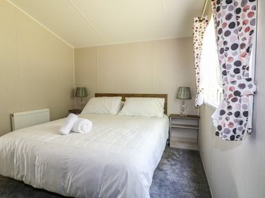 A bedroom with a bed bedside tables lamps and polka dot curtains at Stork Lodge in Swannington near Coalville