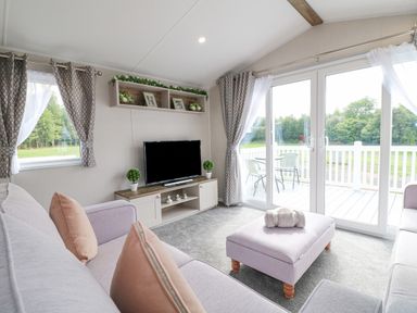 A living room with sofas a television and sliding glass doors opening to a patio at Stork Lodge in Swannington near Coalville