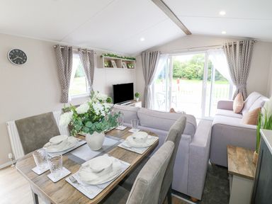A dining table set with plates and glasses next to a living area with a television and sofas at Stork Lodge in Swannington near Coalville
