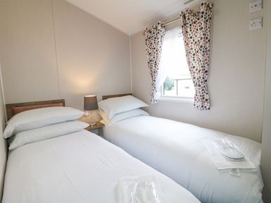 A bedroom with two single beds side by side a lamp on a nightstand and a window with patterned curtains at Stork Lodge in Swannington near Coalville
