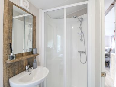 A bathroom with a shower enclosure a sink with a faucet a mirror with a wooden frame and a small shelf at Stork Lodge in Swannington near Coalville