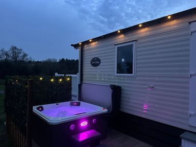 An outdoor hot tub next to a white mobile home with string lights at Stork Lodge in Swannington near Coalville
