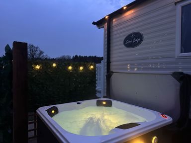 An outdoor hot tub with bubbling water next to a lodge with string lights at Stork Lodge in Swannington near Coalville
