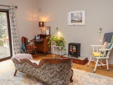 A sitting room with vintage sofa a wooden desk two chairs a small electric fireplace and a plant at Pink Granite Garden of Ireland near Tinahely County Wicklow