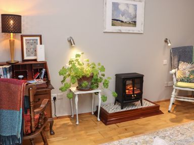 A room with a wooden desk and chair a plant on a small table an electric stove and an armchair with cushions near Pink Granite Garden of Ireland near Tinahely County Wicklow