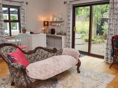 A living room with an antique sofa a side table with a lamp and coffee making area and sliding glass doors leading to a garden at Pink Granite Garden of Ireland near Tinahely County Wicklow