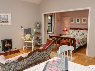 A room with a bed floral bedspread wooden furniture a fireplace a bookshelf and chairs at Pink Granite Garden of Ireland near Tinahely County Wicklow