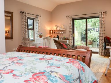 A bedroom with floral bedspread a seating area with chairs a small table and a lounge chair and sliding glass doors leading to a garden at Pink Granite Garden of Ireland near Tinahely County Wicklow
