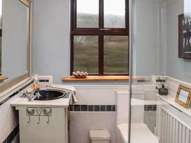 A bathroom with a sink cabinet a mirror a window a toilet and a small trash bin at Pink Granite Garden of Ireland near Tinahely County Wicklow