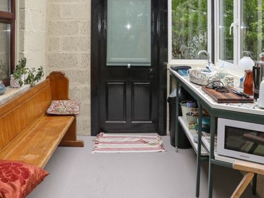 A small kitchen area with a wooden bench and cushions a black door and a countertop with a microwave and sink at Pink Granite Garden of Ireland near Tinahely County Wicklow