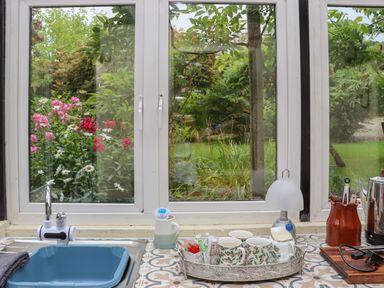 A kitchen sink with blue basin and faucet next to a tray with cups and condiments on a tiled countertop by a window with garden view at Pink Granite Garden of Ireland near Tinahely County Wicklow