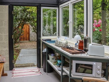A kitchen area with a microwave toaster and sink next to a door leading to a garden at Pink Granite Garden of Ireland near Tinahely County Wicklow