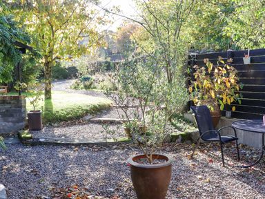 An outdoor garden area with potted plants a black chair and table gravel ground and trees at Pink Granite Garden of Ireland near Tinahely County Wicklow