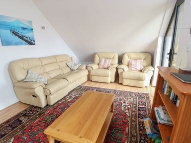 A living room with beige leather sofa and armchairs a wooden coffee table a bookshelf and a painting on the wall at Dunes in Rhosneigr