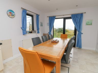 A dining room with a wooden table surrounded by gray and orange chairs and blue curtains at Dunes in Rhosneigr