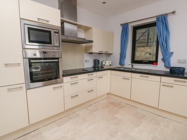 A kitchen with built in oven microwave stovetop blue curtains on a window and countertop appliances at Dunes in Rhosneigr