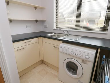 A utility room with a washing machine sink countertop and shelves at Dunes in Rhosneigr