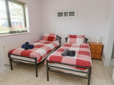 A bedroom with two single beds with red and white checkered bedding and towels on them next to a window and bedside table at Dunes in Rhosneigr