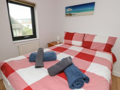 A bedroom with a red and white checkered bedspread and rolled towels on the bed at Dunes in Rhosneigr