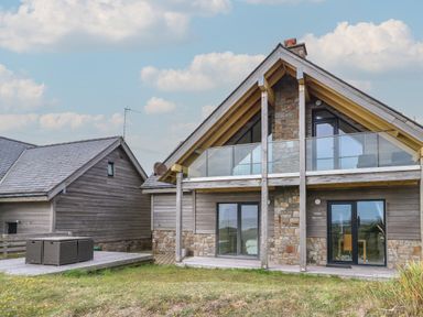 A modern house with wooden and stone exterior with glass balcony and sliding doors at Dunes in Rhosneigr