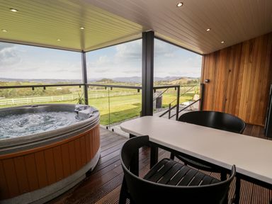A covered outdoor patio with a hot tub a white table and black chairs overlooking a green landscape at Enia Lodge 2 Llanelidan near Corwen